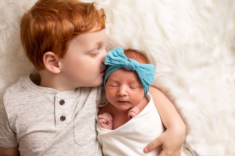 big brother kisses new baby sister on her forehead